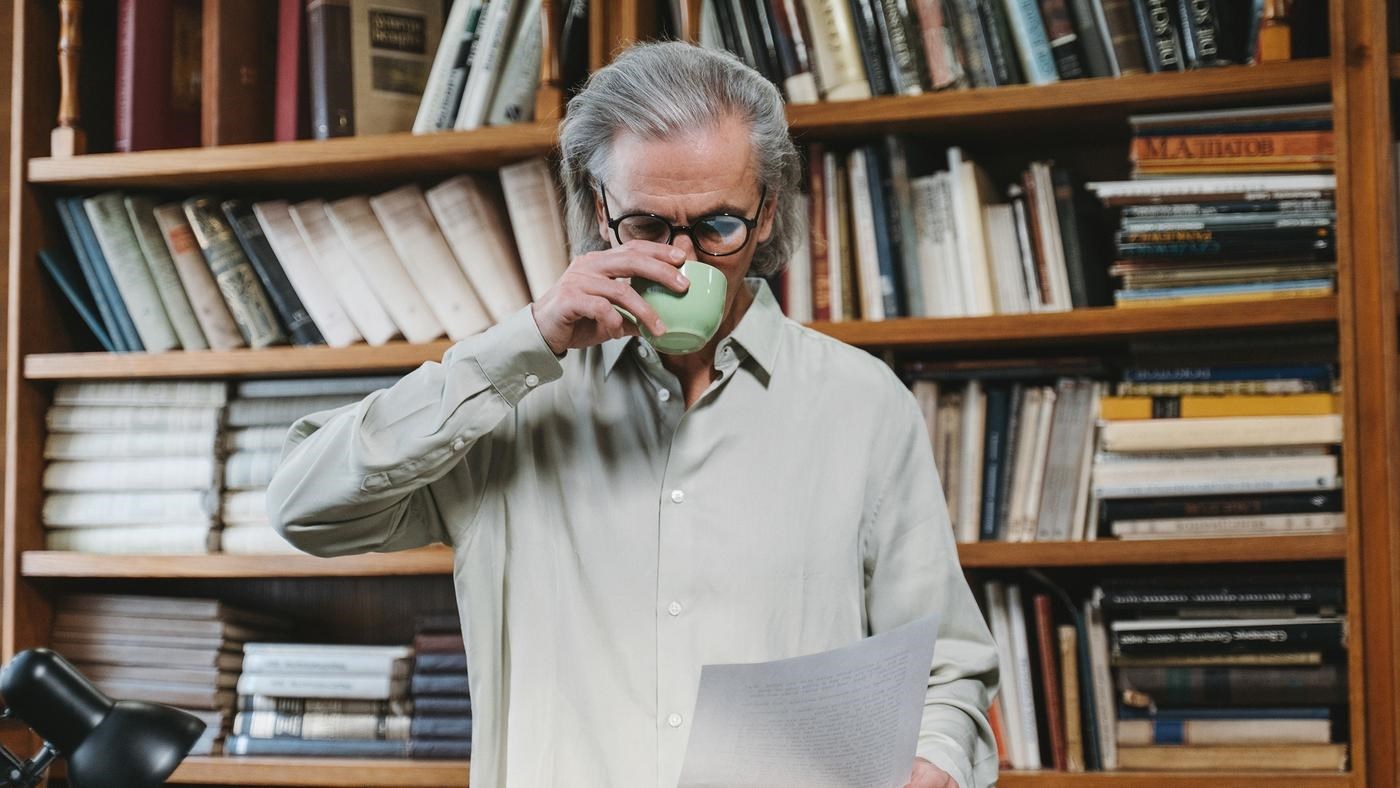 Man sipping coffee and reading in a library