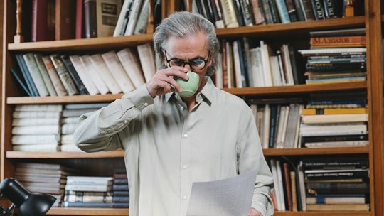 Man sipping coffee and reading in a library