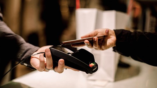 Close-up of people making payment transaction using mobile phone and terminal